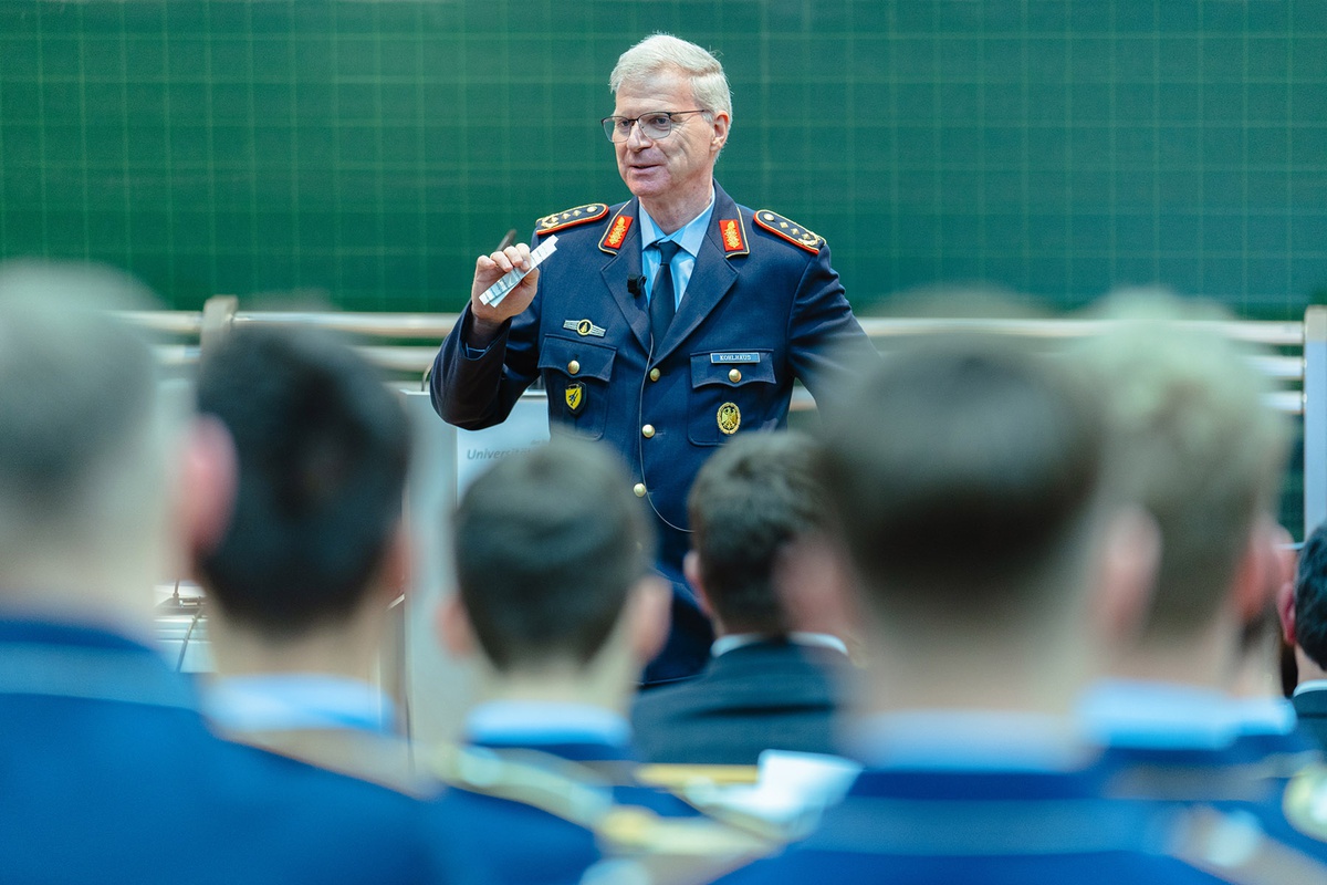 Der Generalleutnant spricht vor einer Gruppe Soldatinnen und Soldatinnen im Audimax. Die Soldatinnen und Soldaten sind von hinten zu sehen, Generalleutnant Kohlhaus steht vor der Gruppe, in seinem Rücken eine Tafel.