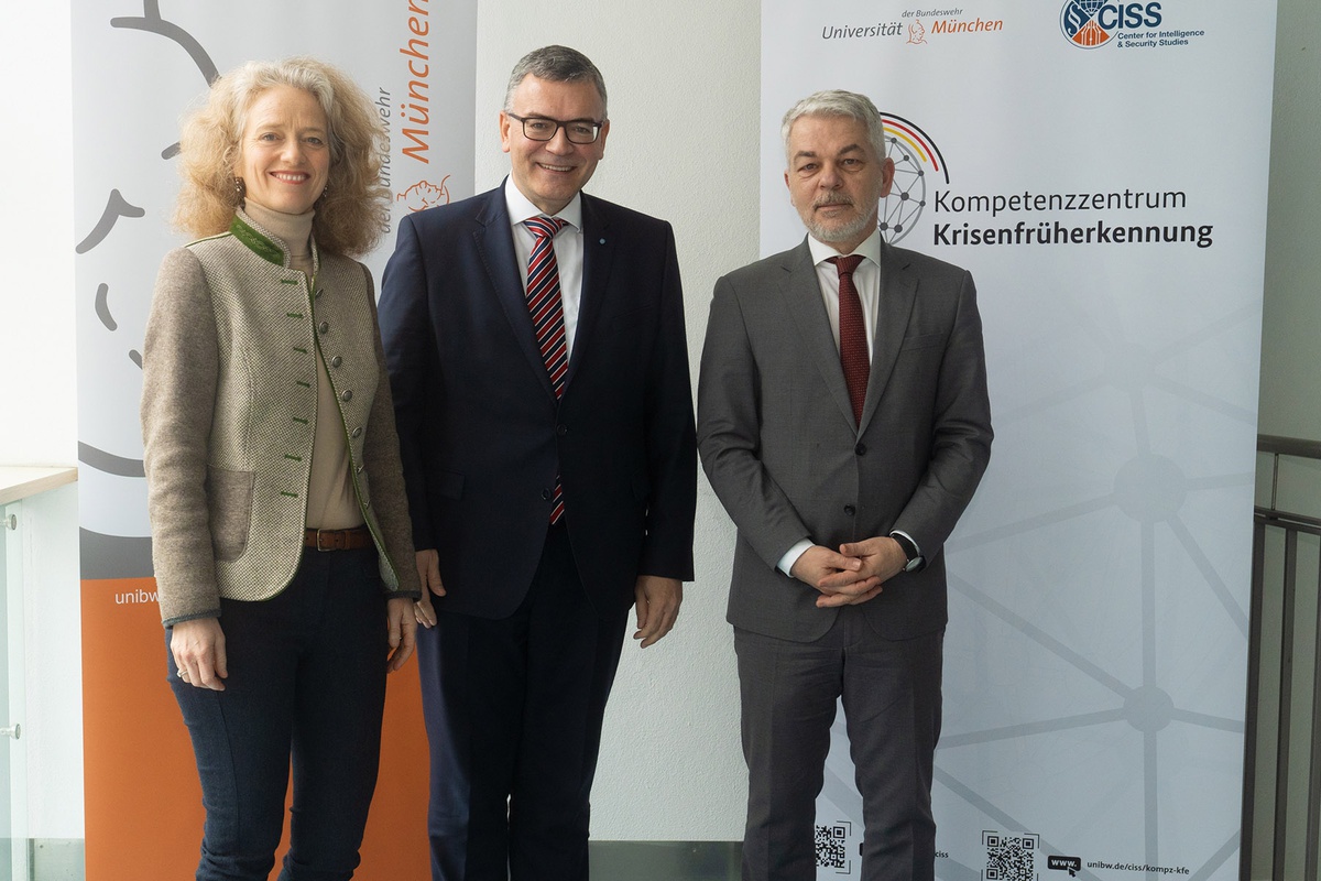 Im Bildhintergrund zwei Banner (links die Athene der UniBw M, rechts das Logo des Kompetenzzentrums), im Vordergrund von links nach rechts Prof. Eva-Maria Kern, Staatsminister Florian Herrmann, Prof. Carlo Masala