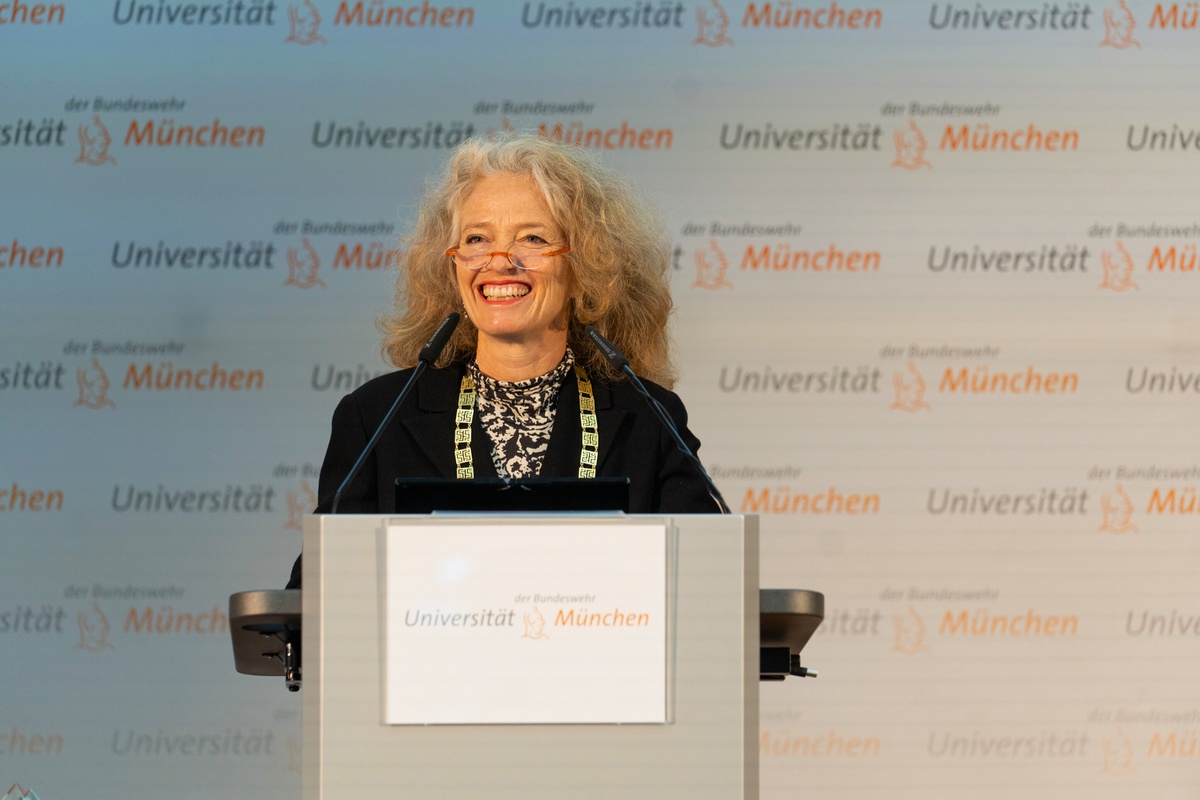 Präsidenting Eva-Maria Kern steht hinter einem Rednerpult und lacht erfreut das Publikum an.