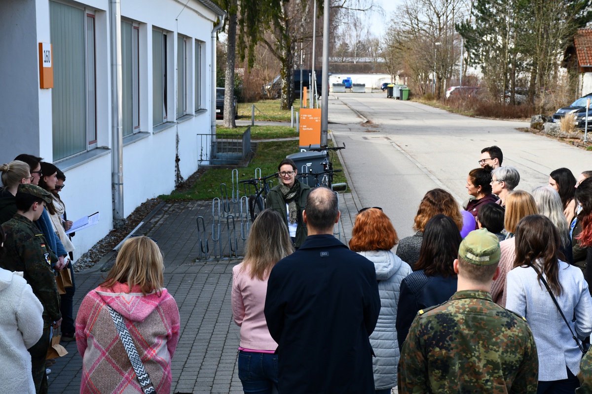 Prof Annette Schmidt steht vor einer großen Gruppe an Menschen, die in einem Halbkreis vor ihr stehen und redet.