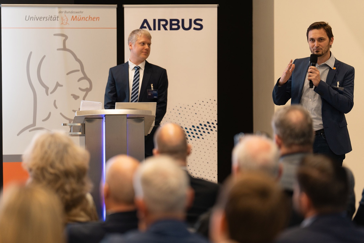 Marcus Knüpfer, Geschäftsführer des FI CODE rechts im Bild zu sehen mit einem Mikrofon in der Hand, sowie Dr. Andreas Stock von Airbus, linksseitig hinter dem Stehpult zu sehen