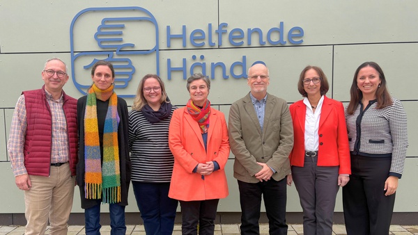 Verschiedene Personen vor dem Logo der Helfenden Hände
